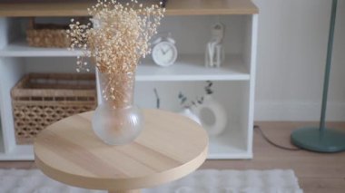 Kurumuş çiçekli küçük bir vazo yaşayan bir yerde, ahşap bir masada duruyor..