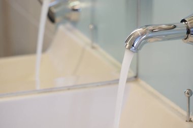 Su musluktan beyaz bir lavabo lavabosuna akıyor..