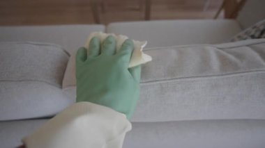 Bir kişi oturma odasındaki kanepeyi bir bez kullanarak siler..