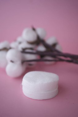 Yuvarlak beyaz bir nesne pembe bir yüzeyde pamuk çiçeklerinin yanında durur..