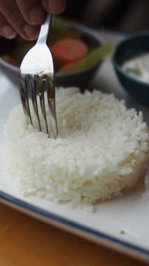 Bir el çatalla pirinci bir tabakta yiyecekle keser..