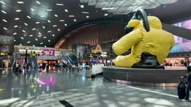 İnsanlar havaalanında büyük sarı bir heykelin etrafında dolaşıyorlar..