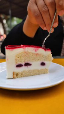 Kafe ortamında insan kırmızı beyaz pastadan bir ısırık alır..