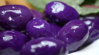 Mor meyveler, yeşil yapraklı beyaz bir tabakta yakından gösterilir..