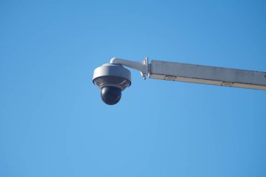 Açık mavi gökyüzünün altındaki direğe bir güvenlik kamerası monte edilmiştir..