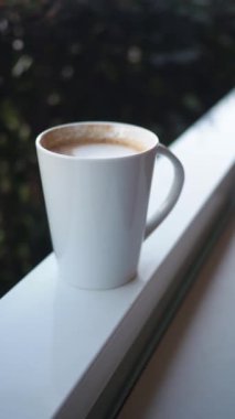 Bir fincan kahve güneşin altında bir çıkıntının üzerinde duruyor. Gün aydınlık görünüyor.