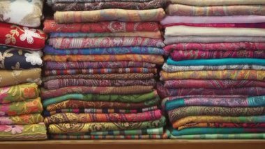 Farklı renk ve desenlere sahip kumaşlar bir dükkanda raflarda duruyor..