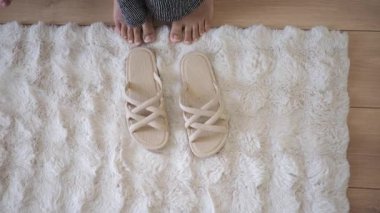 Ayaklarının yanındaki sandaletlerle yumuşak bir halının üzerinde duran bir insan.