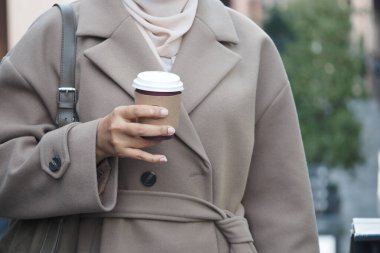 Bir insan gündüz vakti şehir caddesinde yürürken bir bardak tutar..