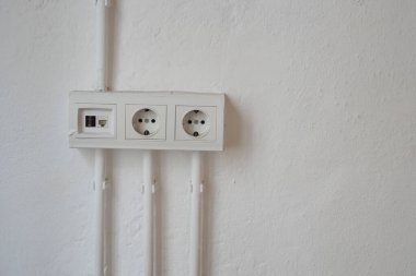 Düz beyaz bir duvarda üç tane elektrik prizi var..