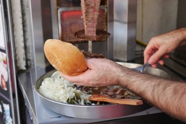 Bir adam büfede et ve malzeme eklerken ekmek tutuyor..