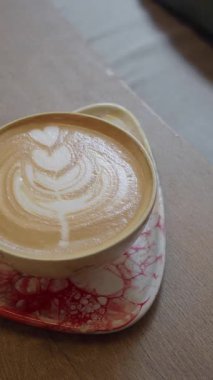Kafedeki bir masada üzerinde güzel sanat eserleri olan sıcak bir fincan latte duruyor..