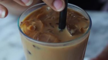 Buzlu kahveyi kamışla karıştıran kişi bardağı tutar..