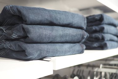 Bir mağazanın rafında düzgünce dizilmiş kot pantolonlar var..