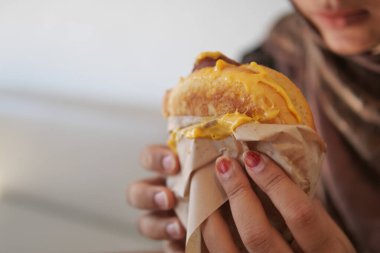 Bir kadın kafeteryada otururken elinde yiyecek bir şey tutuyor..