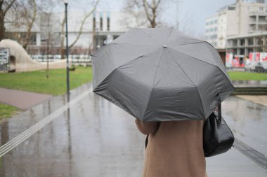 Islak bir kaldırımda elinde şemsiyeyle yürüyen bir insan..