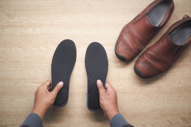 Tahtadaki kahverengi deri ayakkabıların yanında siyah taban tutan eller..