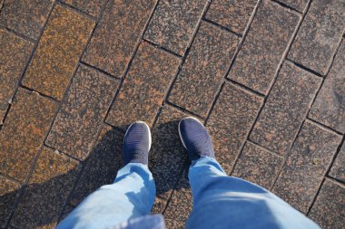 Bir insan gün ışığında mavi ayakkabılar giyerek taştan bir yolda duruyor..