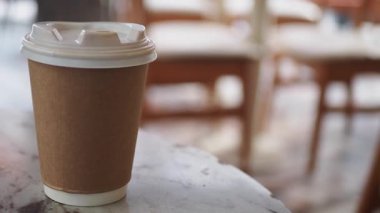 Yoğun bir kafe atmosferinde masanın üzerinde bir fincan kahve duruyor..