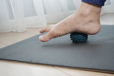 Bir insan evdeki bir paspasın üzerinde ayağını bir masaj topuna yuvarlar..