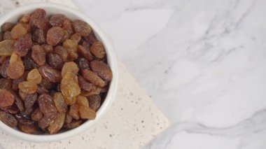 Bir kase açık mermer yüzeyde birçok kuru üzüm barındırır..