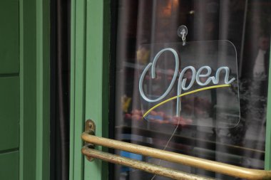 Gün ışığında açık bir tabela bir mağazanın yeşil kapısına asılır..