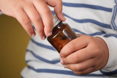 Bir çocuk içinde haplar olan küçük kahverengi bir şişeyi kavrıyor..