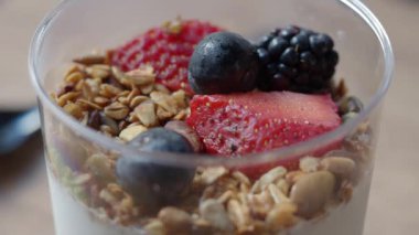 Kişi, üzerinde granola ve taze böğürtlen olan bir kase yoğurt hazırlar..