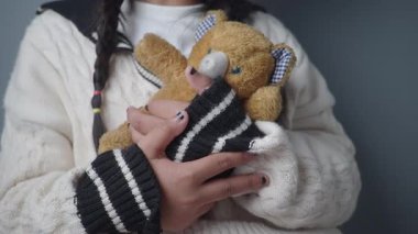 Bir çocuk, ayıcığa sıcacık giysiler giyerken sarılır..