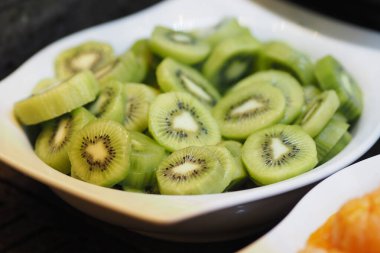 Taze yeşil kivi dilimleri beyaz bir tabakta güzelce sıralanır..