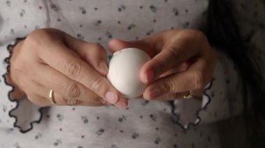 Bir insan yemek yapmaya hazırlanırken iki elinde de beyaz bir yumurta tutar..