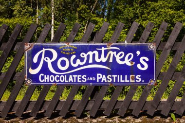 Rowntree 'nin çikolataları ve pastilleri için eski tarz teneke reklam panosu İngiltere' deki Grosmont istasyonunda boyalı ahşap çitlerde sergileniyordu..