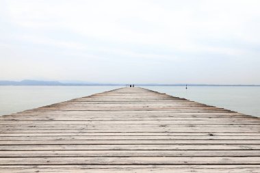 Oturan bir çifte ahşap iskele manzarası. İskele, İtalya 'nın kuzeydoğusundaki Garda Gölü kıyısındaki Sirmione tatil köyünün yanında yer almaktadır..