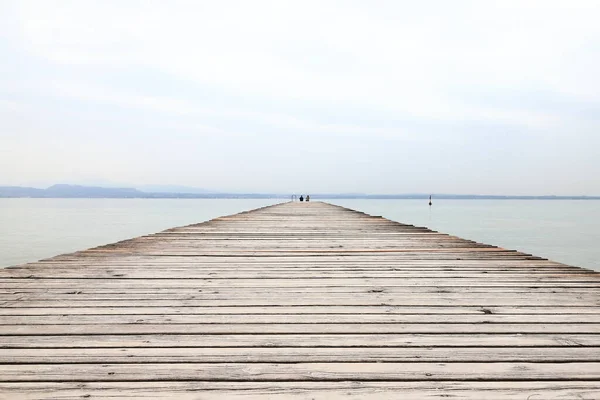 Oturan bir çifte ahşap iskele manzarası. İskele, İtalya 'nın kuzeydoğusundaki Garda Gölü kıyısındaki Sirmione tatil köyünün yanında yer almaktadır..