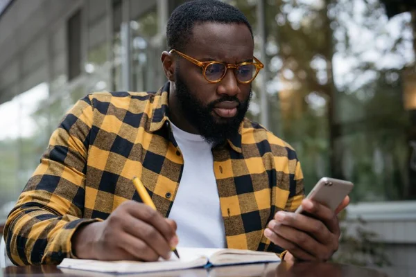 Homem Afro Americano Pensativo Usando Telefone Celular Tomando Notas Trabalhando — Fotografia de Stock