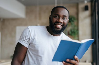 Kitap okuyan mutlu bir Afrikalı Amerikalının portresi. Gülümseyen öğrenci çalışıyor, dil öğreniyor, kameraya bakıyor.