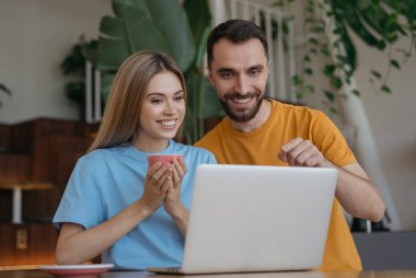 Genç çift dizüstü bilgisayar kullanıyor, evde online alışveriş yapıyorlar. Gülümseyen adam ve kadın görüntülü görüşme yapıyor, internetten iletişim kuruyorlar. Video yayınlayan blogcular 