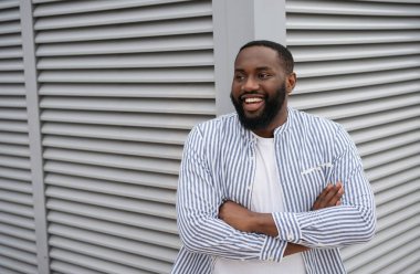 Kollarını kavuşturmuş, gülerek sokakta duran kendine güvenen Afro-Amerikan genç adamın yakın portresi. Başarılı bir iş.   