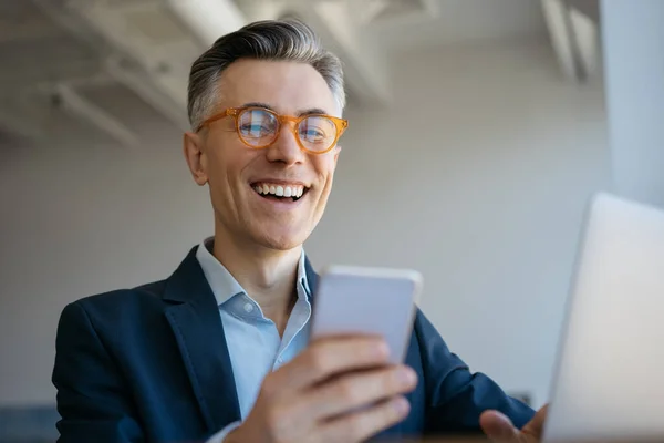 Usmívající Dospělý Muž Používající Notebook Držící Mobilní Telefon Moderní Kanceláři — Stock fotografie