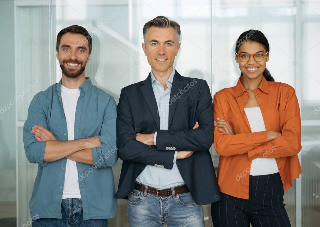 Portrait of happy business people with arms crossed in modern office. Confident multiracial colleagues standing together looking at camera, smiling. Startup team, successful business concept   