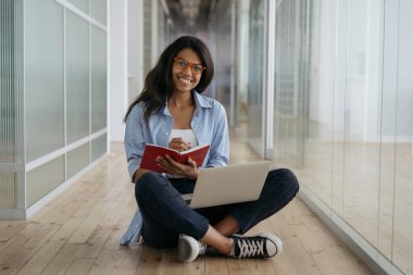 Öğrenci eğitimi, sınav hazırlığı, uzaktan öğrenme, eğitim konsepti. Güzel gülümseyen Afro-Amerikan kadın dizüstü bilgisayar kullanıyor, internette notlar alıyor yerde oturuyor. 