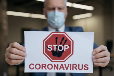 Koruma maskesindeki kıdemli adam elinde Coronavirus posterini tutuyor, seçici odaklanma 