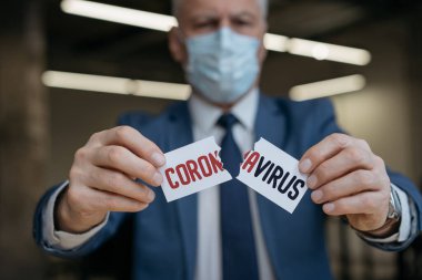 Korumadaki kıdemli adam yüz maskesi yırtma kağıdını kelime koronavirüsü ile yırtıyor, seçici odaklanma. Virüs kavramını durdur