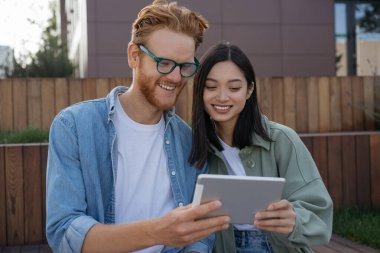 Gülümseyen arkadaşlar dijital tablet kullanıyor, video izliyor, online alışveriş yapıyor, dışarıda oturuyorlar. Öğrenciler birlikte okuyorlar, uzaklık öğrenimi, eğitim kavramı 