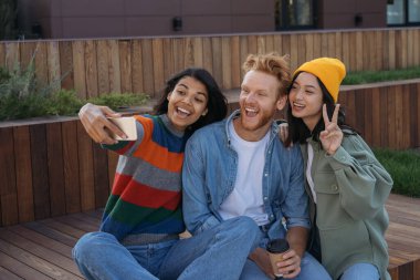 Gülümseyen çok ırklı arkadaşlar cep telefonu kullanıyor, selfie çekiyor, dışarıda eğleniyorlar. Afrikalı Amerikalı kadın nüfuzlu Mutlu arkadaşlarla video yayınlıyor