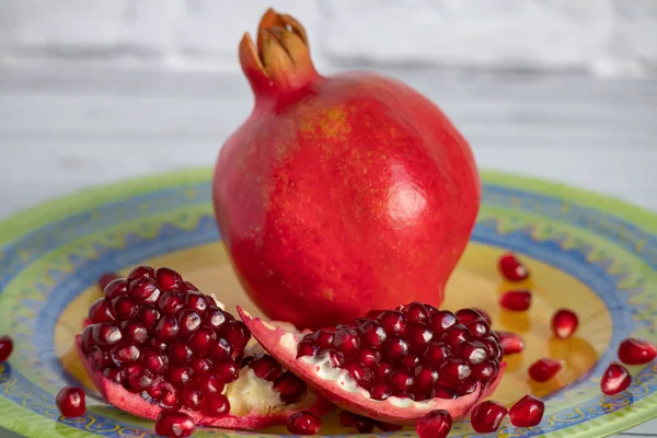 Čerstvé zralý granátové jablko leží na jasném krásném talíři. řez granátového jablka a jeho semena jsou roztroušena na talíři. — Stock fotografie
