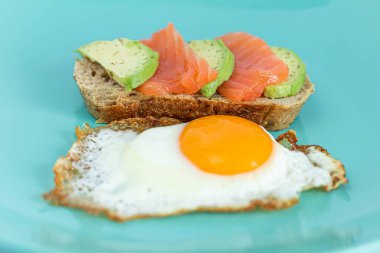 Somonlu ev yapımı tost sandviçi ve bir dilim mısır gevreği ekmeğine avokado. Nane arkaplanlı yumurta sarısı.