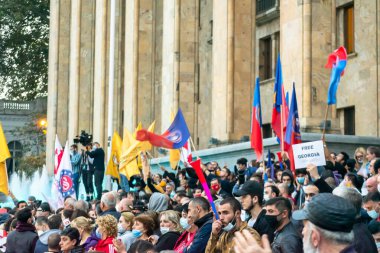 1 Kasım, 2020. Tiblis. Gürcistan Cumhuriyeti. Seçim sonrası protesto sırasında parlamento binasının önünde posterleri ve bayrakları olan kalabalık.