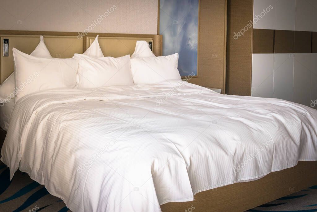 King sizes bed  with brown interior and white bright clean sheets and six pillows comfort. Luxurious stays and comfort concept.