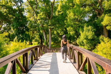 Yeşil ve dev ağaçlarla çevrili bir kadın Brdige 'de yürüyor. Kafkasya 'da gezmek. Dendroloji parkı. Georgia.